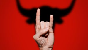 Hand formt die "Devil Horns" im Hintergrund der Schatten eines Stier-Kopfes