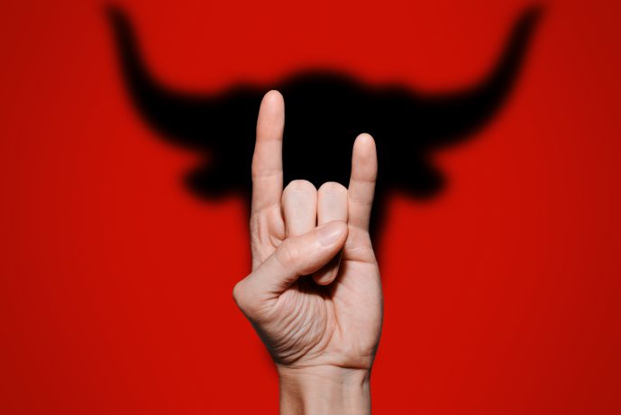 Hand formt die "Devil Horns" im Hintergrund der Schatten eines Stier-Kopfes