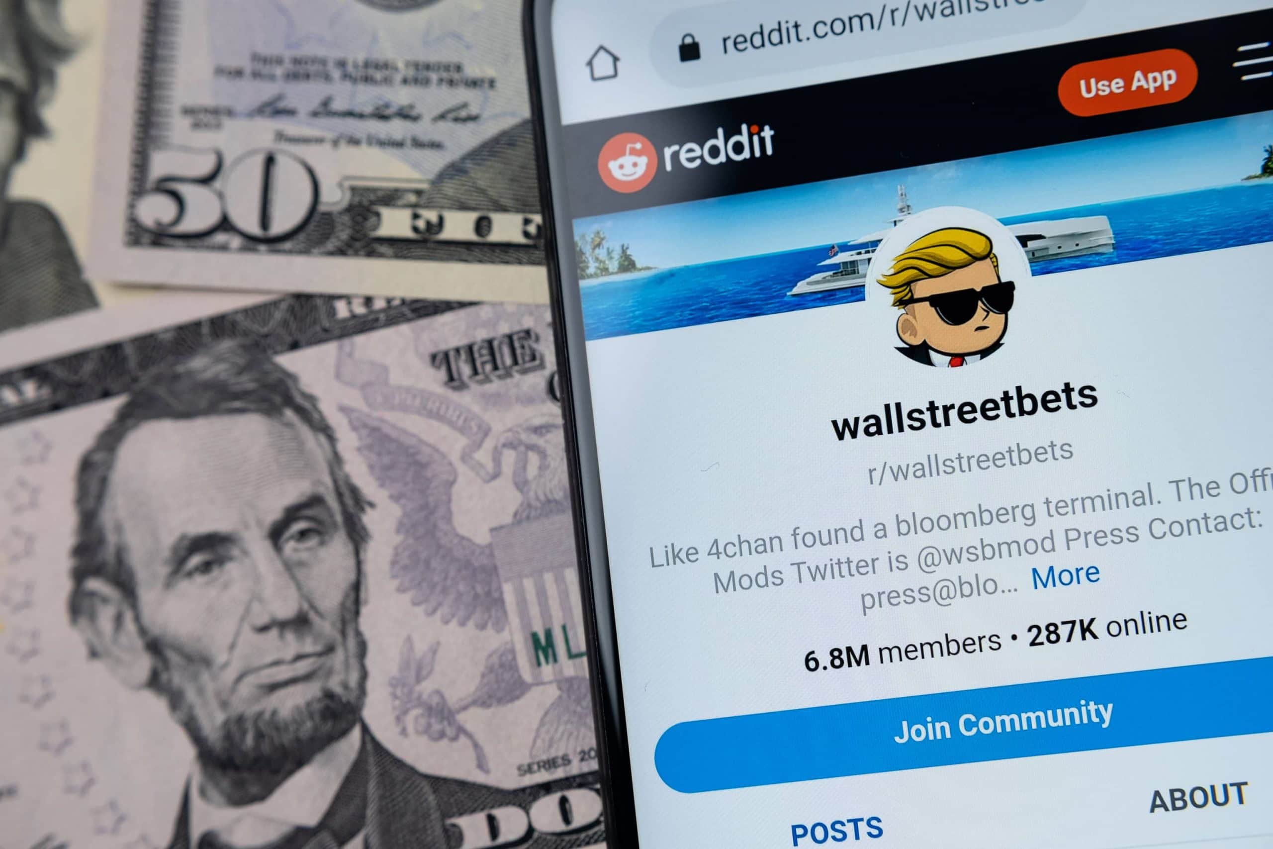 Ein Smartphone-Bildschirm liegt neben mehreren Dollar-Noten. Auf dem Bildschirm ist die Reddit-Seite der WallStreetBets zu sehen.