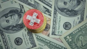 Bitcoin-Münze mit Schweizer Nationalfarben auf Dollar-Scheinen