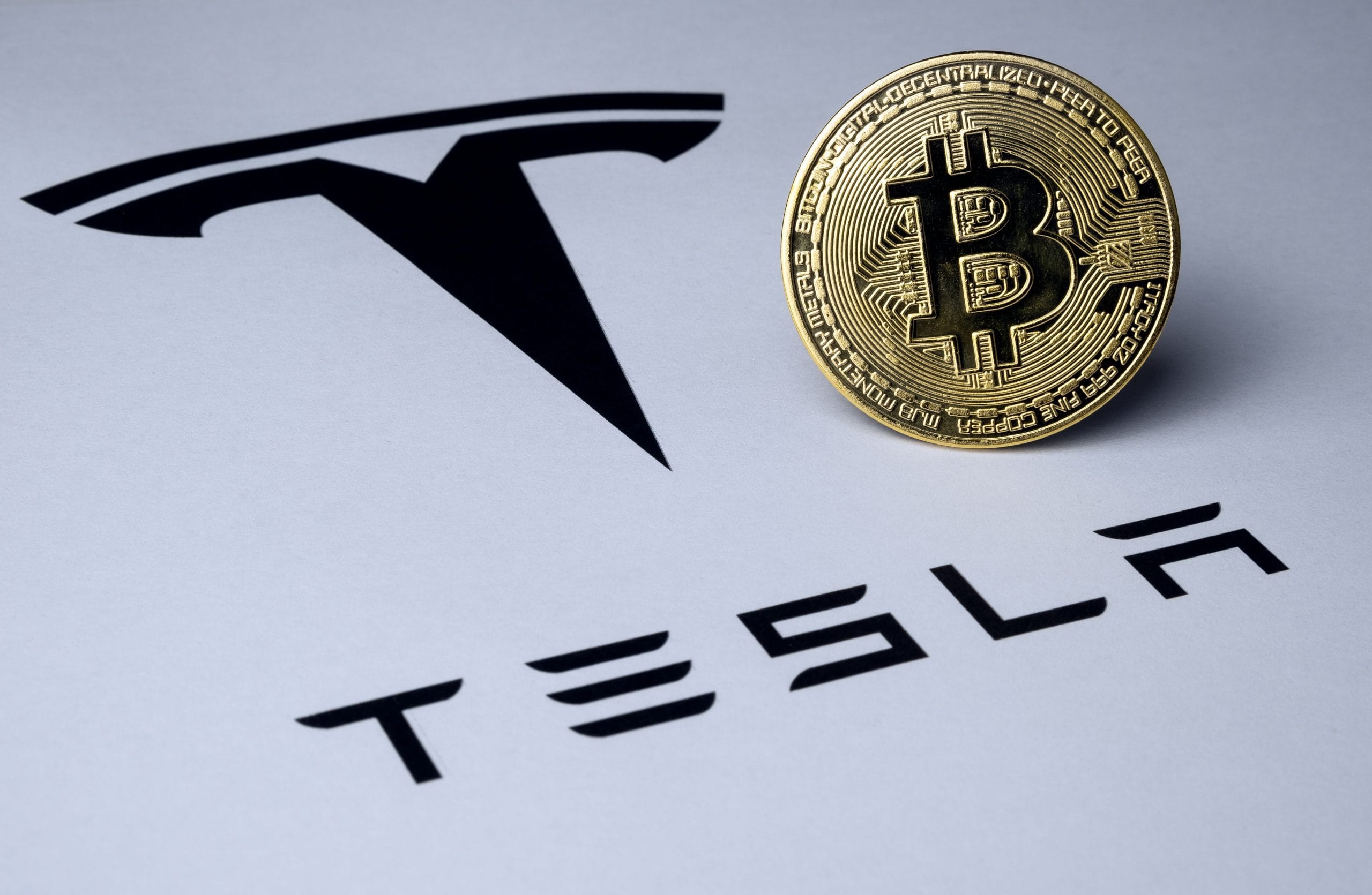 Ein Bitcoin neben dem Logo des US-Autobauers Tesla.