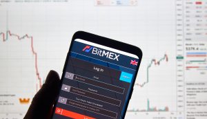 BitMEX Logo auf Smartphone, dahinter ein Kurs-Chart