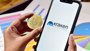 Bitcoin-Münuze neben Smartphone mit Kraken-Logo, im Hintergrund Balken- und Torten-Diagramme