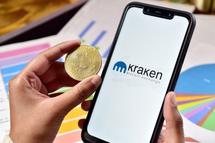 Bitcoin-Münuze neben Smartphone mit Kraken-Logo, im Hintergrund Balken- und Torten-Diagramme