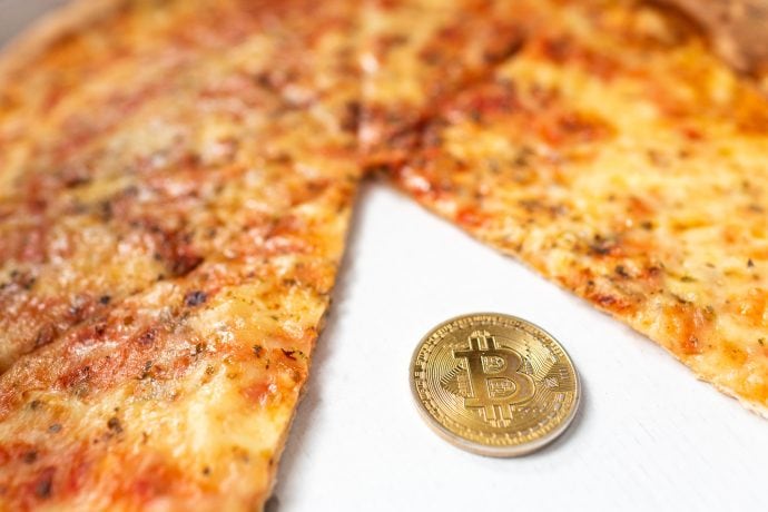 Bitcoin-Münze neben einer geschnittenen Pizza