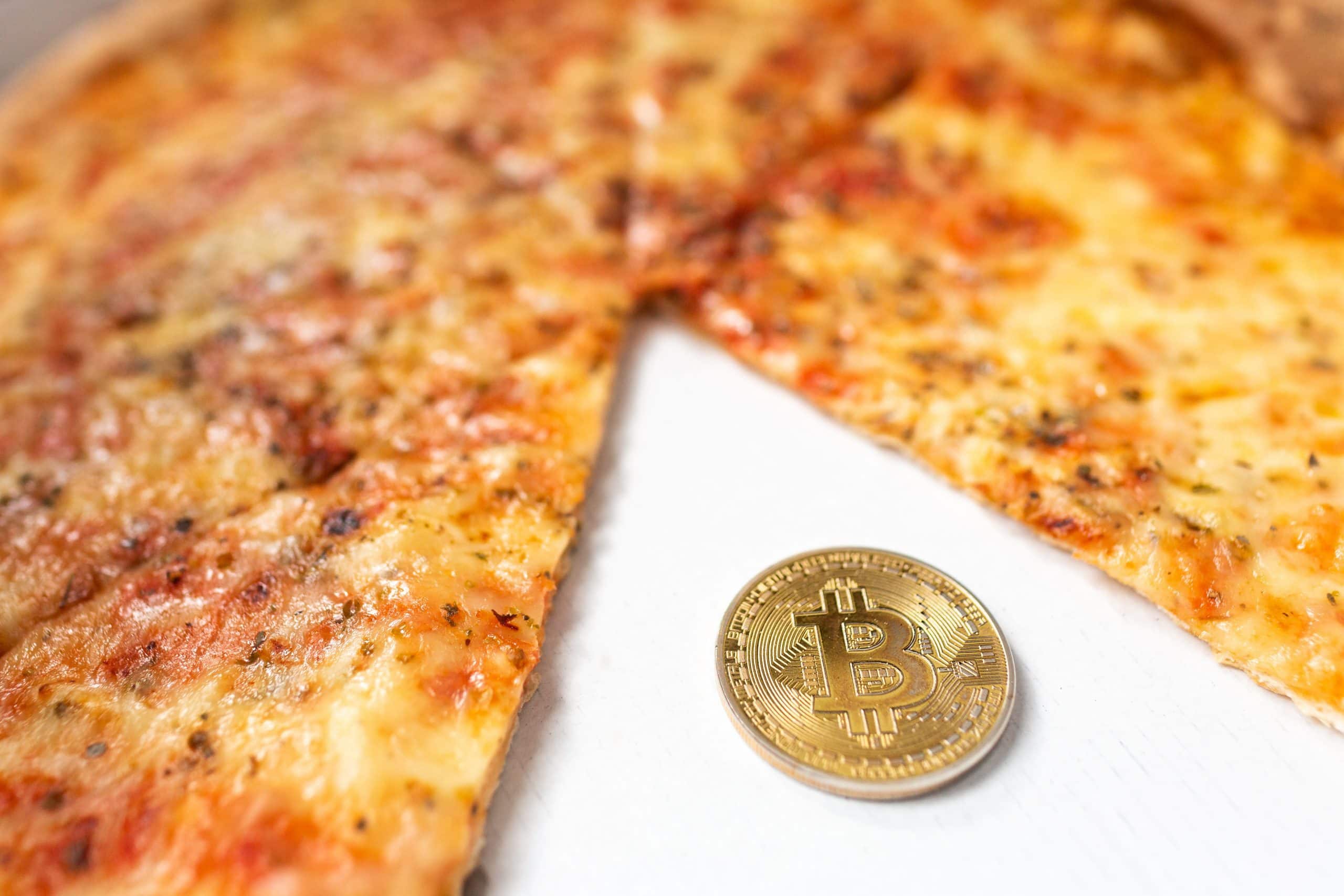 Bitcoin-Münze neben einer geschnittenen Pizza