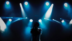 Rapper steht auf der Bühne. Hinter ihm sind Scheinwerfer.
