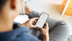 Ein Mann schaut auf sein Smartphone, dort ist die Trade Republic App geöffnet und zeigt ein Depot an.