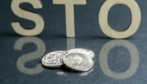 Drei Krypto-Münzen liegen auf einem Tisch. Dahinter stehen die Buchstaben S T O