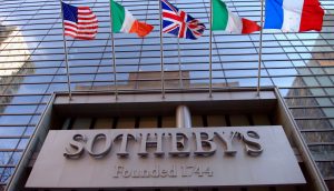 Das Sotheby's-Logo prangt an einer gläsernen Fassade. Darüber wehen die Flaggen der USA, Italiens, Großbritanniens, Irlands und Frankreichs.