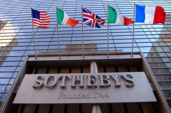 Das Sotheby's-Logo prangt an einer gläsernen Fassade. Darüber wehen die Flaggen der USA, Italiens, Großbritanniens, Irlands und Frankreichs.