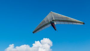 Ein Gleitsegler fliegt durch die Luft. Im Hintergrund ist eine Wolke.