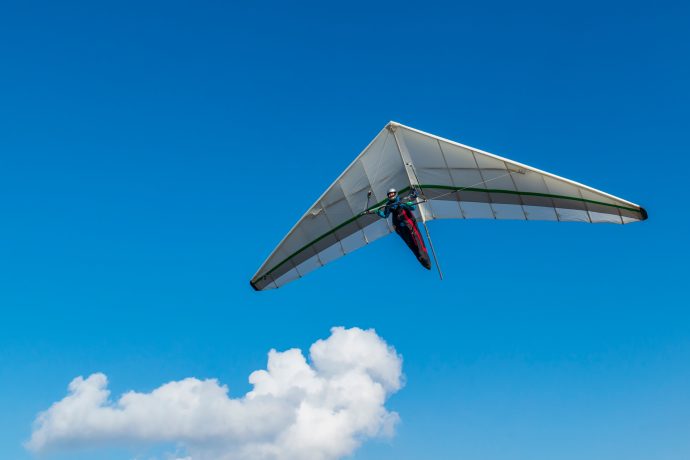 Ein Gleitsegler fliegt durch die Luft. Im Hintergrund ist eine Wolke.