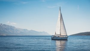 Ein Segelschiff fährt auf stahlendblauem Meer. Am Horizont ist Land in Sicht.