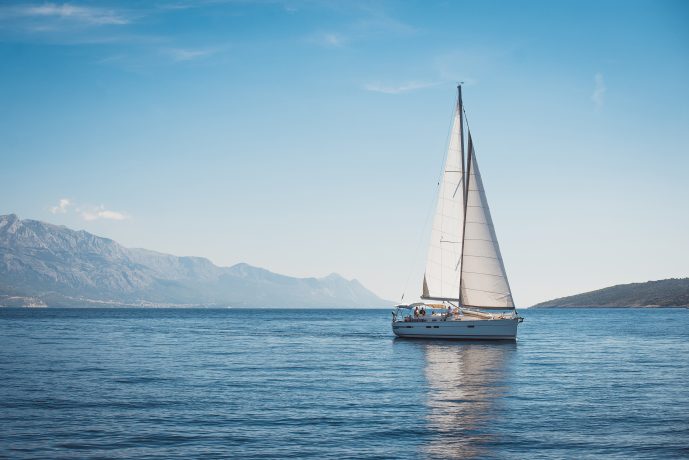 Ein Segelschiff fährt auf stahlendblauem Meer. Am Horizont ist Land in Sicht.