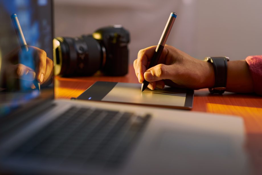 Dieses österreichische NFT-Auktionshaus will hoch hinaus Eine Hand zeichnet etwas auf ein Tablet. daneben steht ein MacBook.