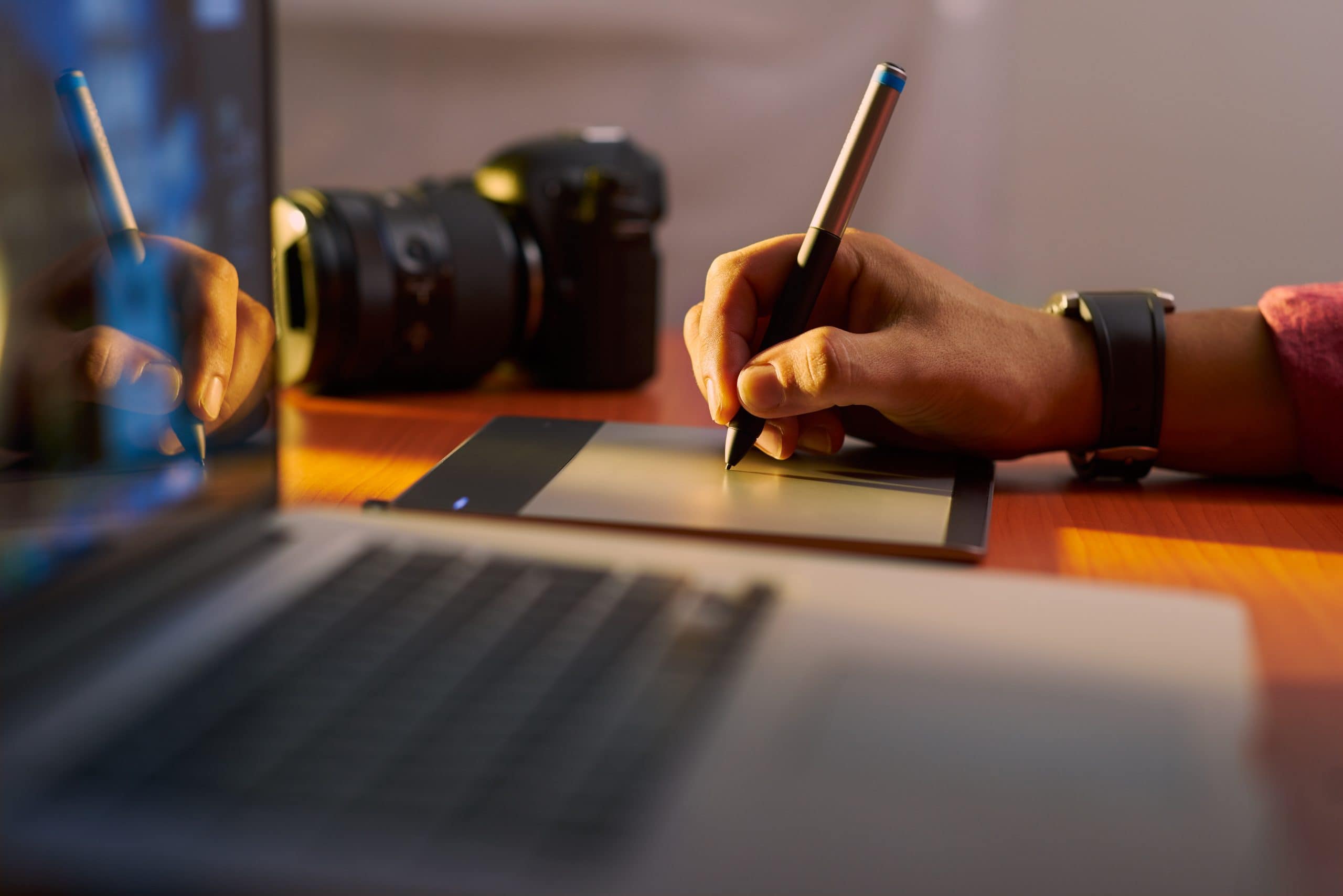 Eine Hand zeichnet etwas auf ein Tablet. daneben steht ein MacBook.