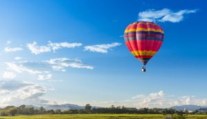 Ein Heißluftballon steigt über einer grünen Landschaft empor.