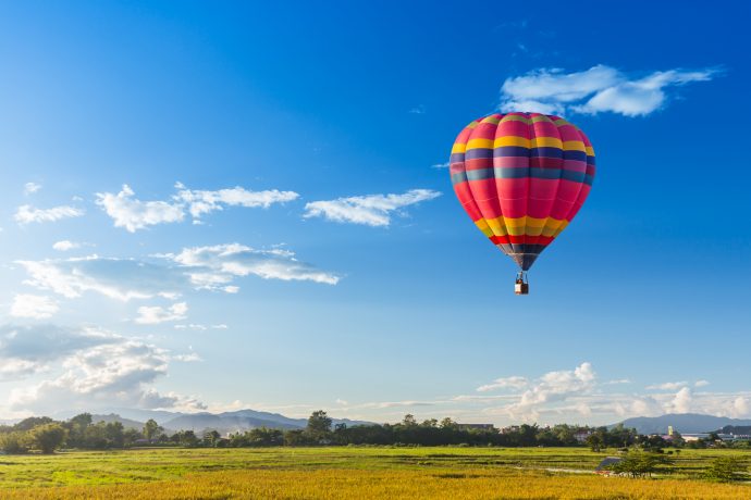 Ein Heißluftballon steigt über einer grünen Landschaft empor.