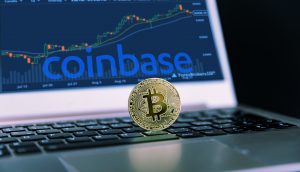 Eine Bitcoin-Münze liegt auf einem Laptop. Dahinter ist Kurs auf der Krypto-Börse Coinbase abgebildet.