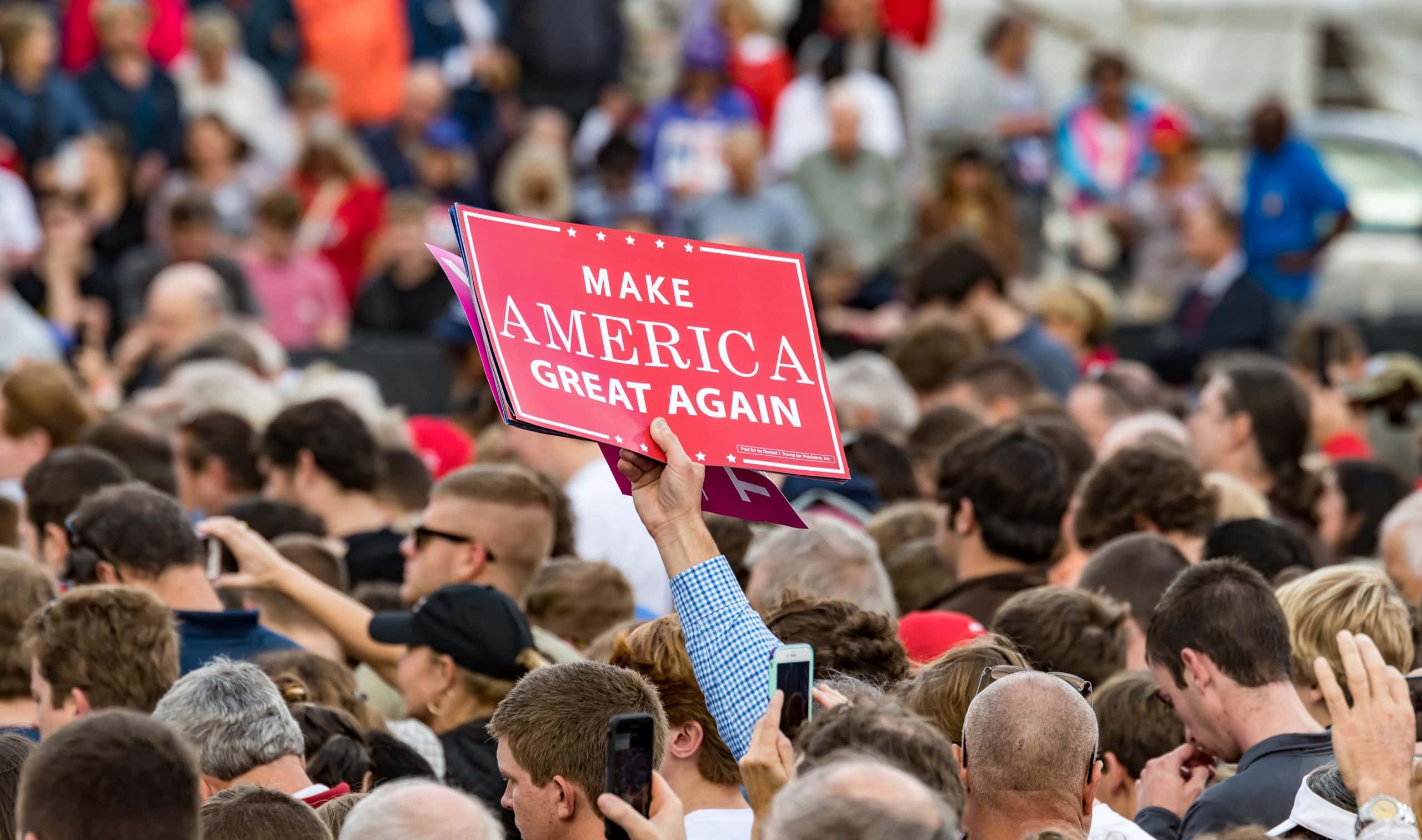 Eine Menschenmenge zieht durch die Straßen. Einer hält ein "Make America Great Again" Schild in die Höhe.