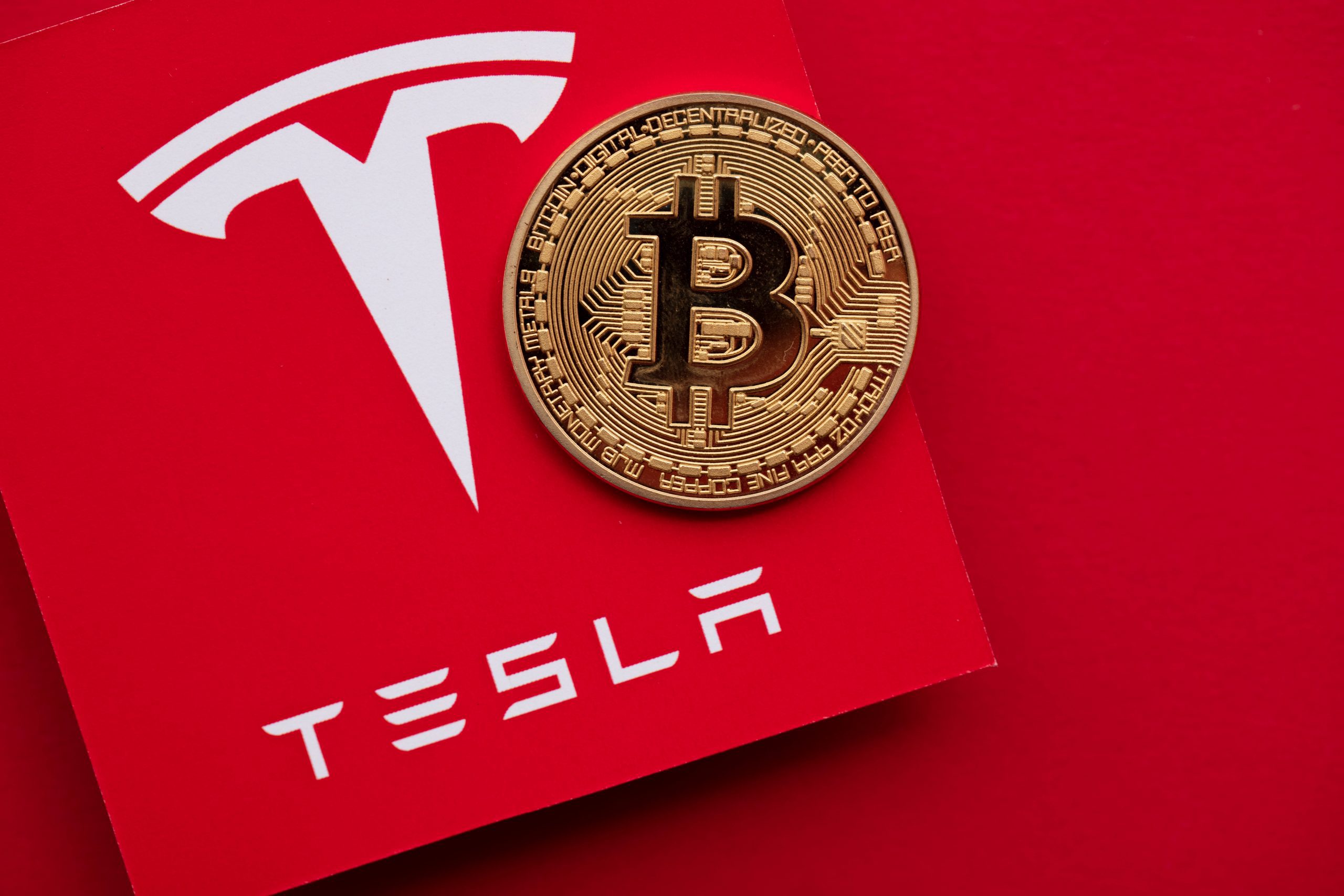 Bitcoin-Münze vor Tesla-Logo