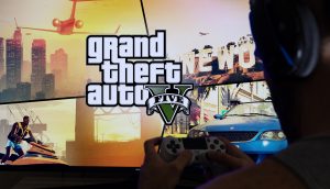 Ein Spieler sitzt vor einem Bildschirm auf dem GTA V zu sehen ist.