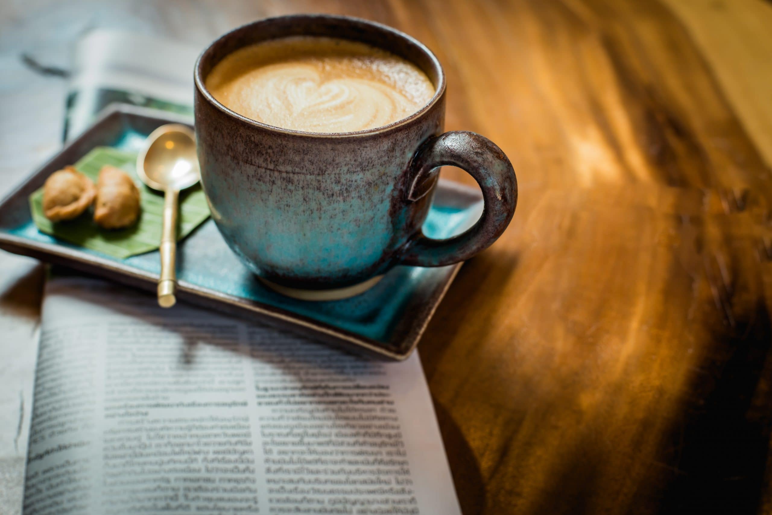 Eine Tasse Kaffee steht auf einem Untersetzer, der auf einer Zeitung steht, die auf einem Holztisch liegt.