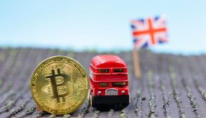 Bitcoin-Münze neben einem Londoner Spiezleugbus, im Hintergrund die Großbritannien-Flagge