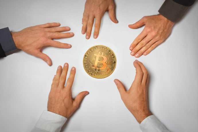 Fünf Hände greifen nach einem Bitcoin –(Symbolbild institutionelles Krypto-Engagement)