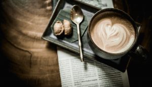 Eine Kaffeetasse steht auf einem Tablett mit Löffel und Keksen, das auf einer Zeitung steht.