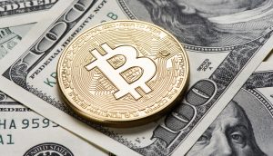 Ein Bitcoin liegt auf einer 100-US-Dollar Note.