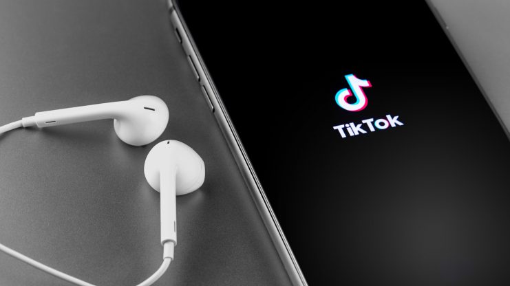 Weiße Kopfhörer liegen neben einem Smartphone mit TikTok-Logo.