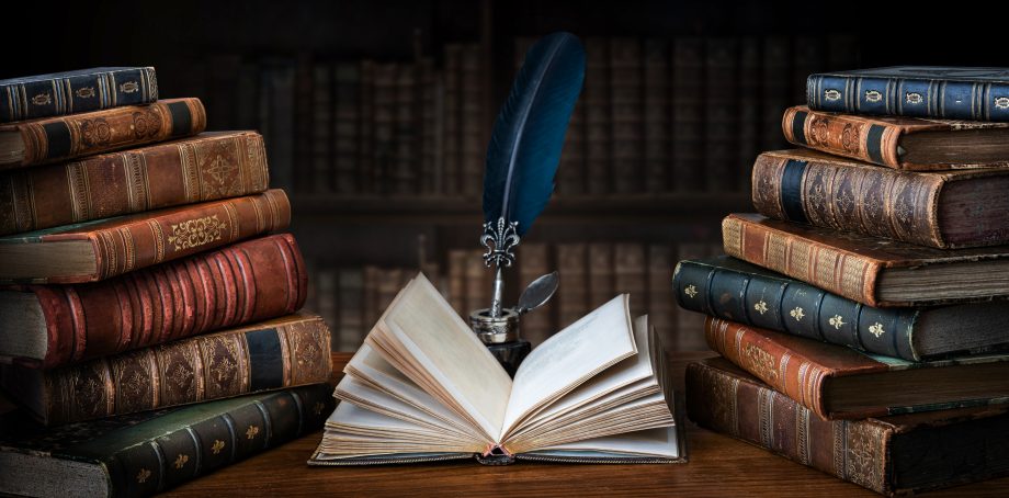 Open book lies on a table, surrounded by stacks of books