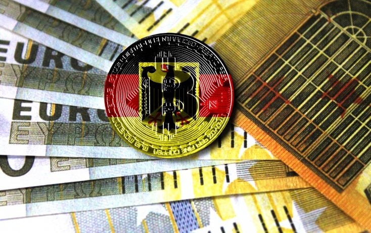 Ein Bitcoin in den Farben Deutschlands liegt auf mehreren Euro-Noten.