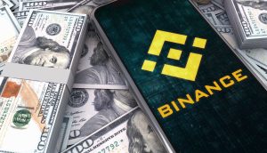 Geldbündel auf denen ein mobiles Endgerät liegt, dass auf der Seite von Binance ist