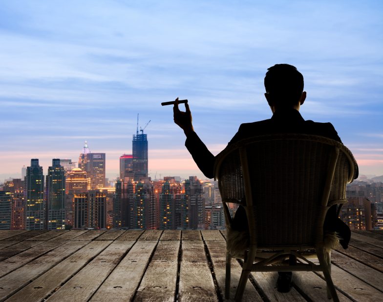 Was machen Investoren mit viel Geld bezüglich Kryptowährungen? Mann mit Zigarre betrachtete Stadt in BlueHour.