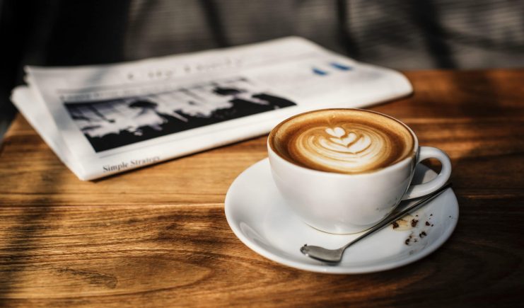 Kaffee und Zeitung auf einem Holztisch.