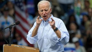 Joe Biden mit entschlossenem Gesichtsausdruck vor amerikanischen Flaggen
