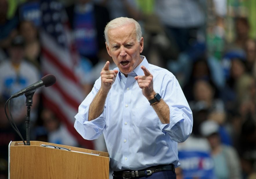 Joe Biden mit entschlossenem Gesichtsausdruck vor amerikanischen Flaggen