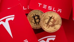 Bitcoin Münzen liegen vor rotem Tesla Logo