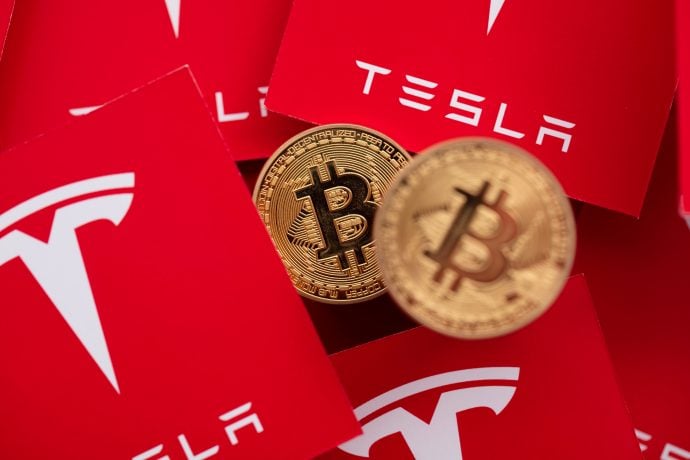 Bitcoin Münzen liegen vor rotem Tesla Logo