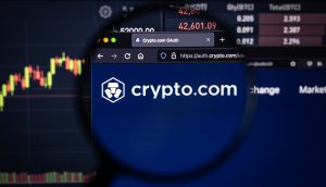 Eine Lupe fokussiert auf das Logo und die Website von crypto.com, die auf einem Computerbildschirm angezeigt werden, eingerahmt von Finanzdiagrammen und dynamischen Marktdaten.