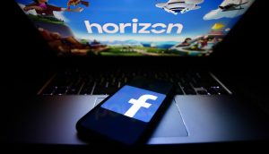 Smartphone mit Facebook-Logo liegt auf Laptop mit Horizon World Ladebildschirm.