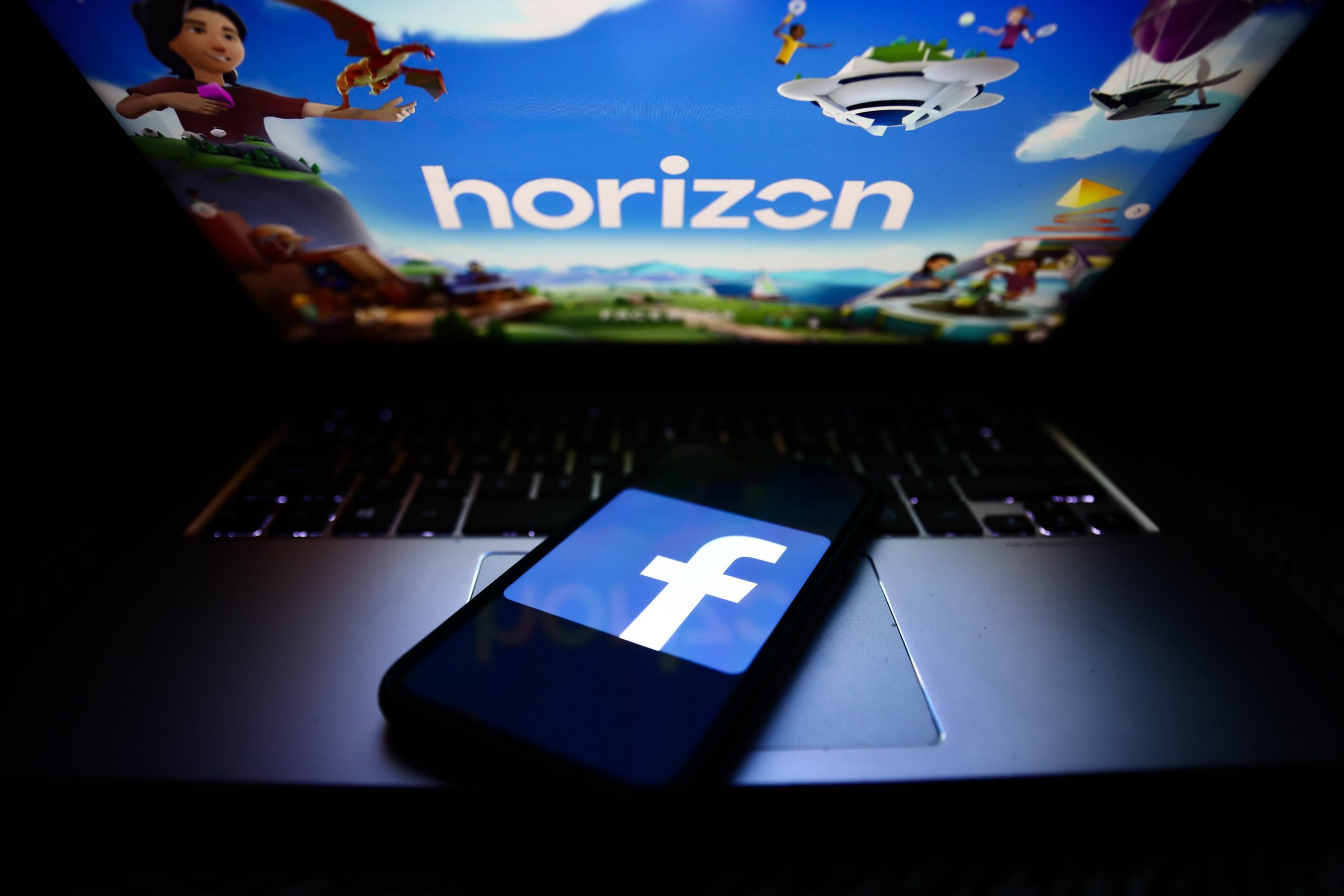 Smartphone mit Facebook-Logo liegt auf Laptop mit Horizon World Ladebildschirm.