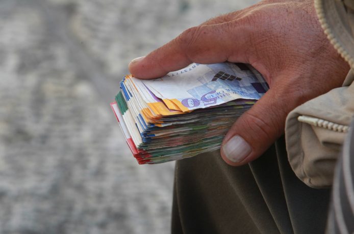 Geldwechsler hält Bündel Schekel in der Hand.