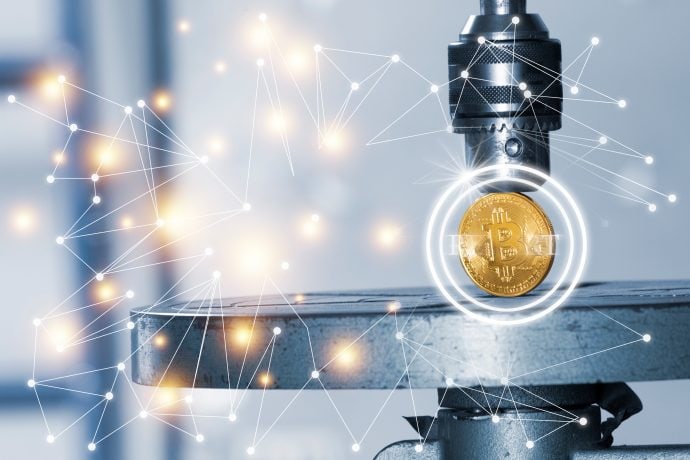 Ein goldener Bitcoin unter einer Metallpresse mit digitaler Netzwerkgrafik-Overlay, der die dynamische Entwicklung von Bitcoin und der Technologie hervorhebt.
