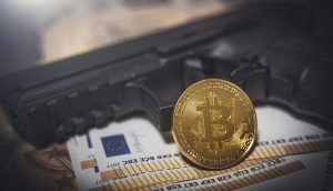 Pistole neben Euro-Noten und Bitcoin-Münze.