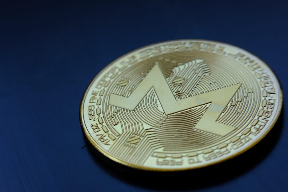 Eine goldene Monero-Kryptowährungsmünze mit dem Monero-Logo liegt auf einer dunkelblauen Oberfläche.