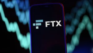 Auf einem Smartphone ist das FTX-Logo vor dem dynamischen Hintergrund blauer und grüner Finanzdiagrammlinien gut sichtbar.